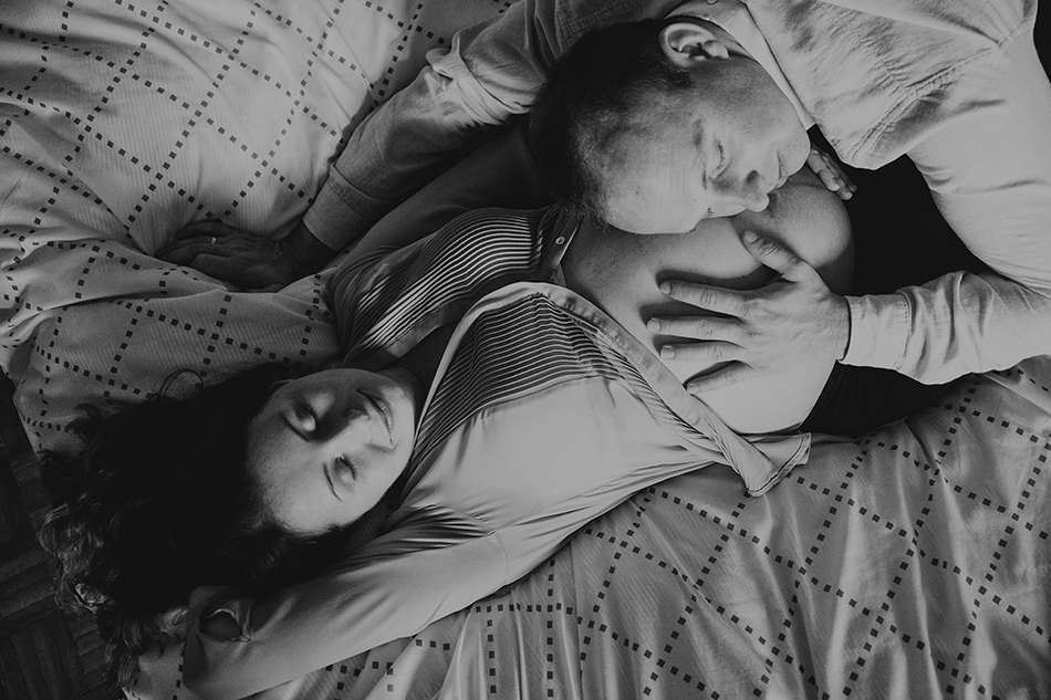 młodzi rodzice leżą na łóżku, mążczyzna przytula się do brzuszka kobiety